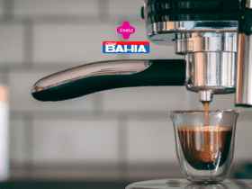 Imagem de uma máquina de café expresso em close-up, enquanto extrai um café em um pequeno copo de vidro. Acima da imagem, estão as logos da Livelo e das Casas Bahia.