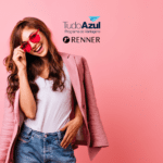 Imagem de uma jovem mulher sorridente, vestindo um blazer rosa e óculos de sol rosados, em um fundo também rosa. Acima da imagem, estão as logos do programa de vantagens TudoAzul e da loja Renner.