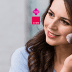 Mulher branca com cabelo castanho, sorrindo enquanto aplica blush no rosto com um pincel de maquiagem. Ao lado, estão os logos da Livelo e da Avon, destacando uma parceria de beleza e cuidado pessoal.
