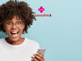 **Texto alternativo:** Imagem de uma mulher jovem e animada, com cabelos cacheados e volumosos, usando óculos redondos e segurando um smartphone. Ela está sorrindo amplamente com expressão de surpresa. Ao fundo, um fundo azul claro e, acima da mulher, estão as logos da Livelo e Ponto Frio.
