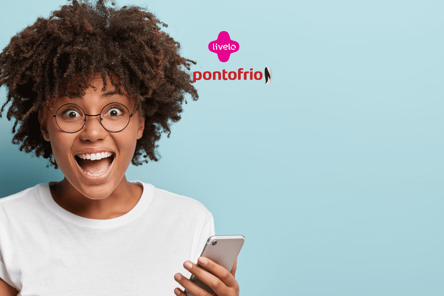 **Texto alternativo:** Imagem de uma mulher jovem e animada, com cabelos cacheados e volumosos, usando óculos redondos e segurando um smartphone. Ela está sorrindo amplamente com expressão de surpresa. Ao fundo, um fundo azul claro e, acima da mulher, estão as logos da Livelo e Ponto Frio.