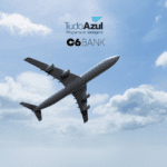 **Texto alternativo:** Imagem de um avião voando em um céu azul com algumas nuvens brancas. Acima do avião, estão as logos do TudoAzul e C6 Bank.