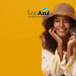 Mulher sorridente com chapéu segurando uma carteira com passagens aéreas, piscando para a câmera. Logotipo do TudoAzul está acima.