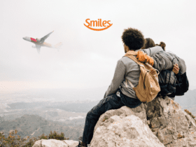 Grupo de amigos sentados em uma rocha, apreciando a vista de um avião que passa ao fundo, envolto por nuvens. Logotipo da Smiles ao topo da imagem.