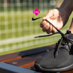 Pessoa amarrando o cadarço de um tênis preto da Nike, em um ambiente de campo de futebol. Acima do tênis, estão os logos da Livelo e da Nike, sugerindo uma parceria voltada para o esporte e estilo de vida ativo.