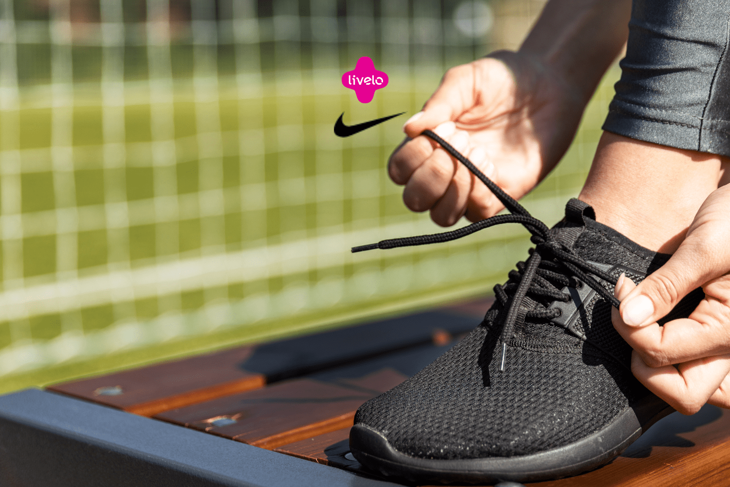 Pessoa amarrando o cadarço de um tênis preto da Nike, em um ambiente de campo de futebol. Acima do tênis, estão os logos da Livelo e da Nike, sugerindo uma parceria voltada para o esporte e estilo de vida ativo.