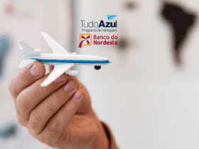 Mão segurando um avião em miniatura com os logotipos do programa de vantagens TudoAzul e do Banco do Nordeste ao fundo.