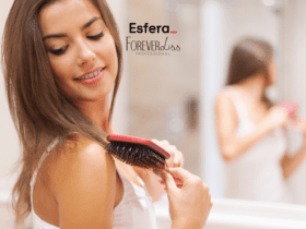 Descrição alternativa curta: Mulher sorridente penteando o cabelo com uma escova vermelha, em frente a um espelho. Na parte superior da imagem, os logotipos da Esfera e Forever Liss Professional.