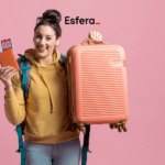 Descrição alternativa curta: Mulher sorridente, vestindo moletom amarelo e mochila verde, segurando uma mala cor de pêssego e um passaporte com passagens. Ao fundo, um fundo rosa e o logotipo da Esfera na parte superior da imagem.