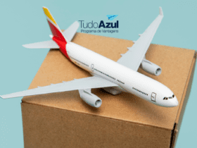 Na imagem, há um modelo de avião em miniatura pousado sobre uma caixa de papelão. O fundo é de cor azul clara, o que destaca o avião e a caixa. No canto superior direito da imagem, está o logotipo do programa de vantagens "TudoAzul", com o texto em azul escuro e um ícone de um avião de papel azul acima do texto. A imagem sugere uma associação entre o programa de fidelidade TudoAzul e a ideia de viagem ou transporte.