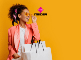 Na imagem, uma mulher sorridente, vestida com um blazer rosa e segurando sacolas de compras, posa contra um fundo amarelo vibrante. Ela está usando óculos de sol amarelos e um lenço colorido amarrado no cabelo, que complementa seu visual moderno e estiloso. No centro superior da imagem, os logotipos da Livelo e da Insider estão visíveis, indicando uma colaboração ou promoção entre as marcas.