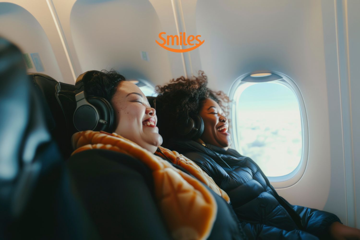 Duas mulheres sentadas em um avião, usando fones de ouvido, estão sorrindo enquanto apreciam o voo. Através da janela, o céu está azul com nuvens brancas. Acima delas, está o logo laranja da Smiles, transmitindo uma sensação de alegria e relaxamento durante a viagem.
