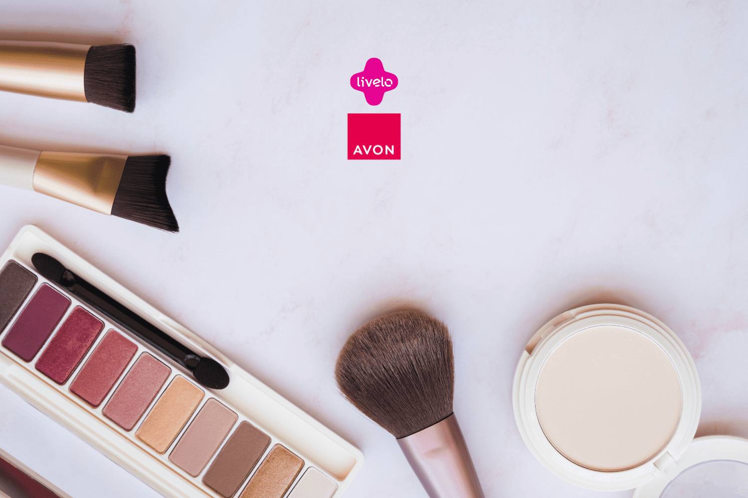 Pincéis de maquiagem, uma paleta de sombras em tons neutros e uma base em pó estão organizados sobre uma superfície clara de mármore. No centro da imagem, estão as logos da Livelo e da Avon.