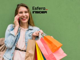 Uma mulher loira está sorrindo enquanto fala ao telefone e segura várias sacolas de compras coloridas. Ao fundo, uma parede verde. Acima dela, estão as logos da Esfera e Insider.