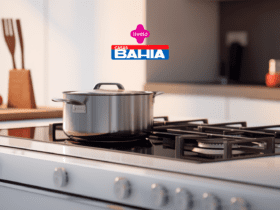 Uma panela de aço inoxidável está sobre um fogão moderno de quatro bocas, em uma cozinha bem iluminada e minimalista. No topo da imagem, aparecem as logos da "Livelo" e "Casas Bahia".