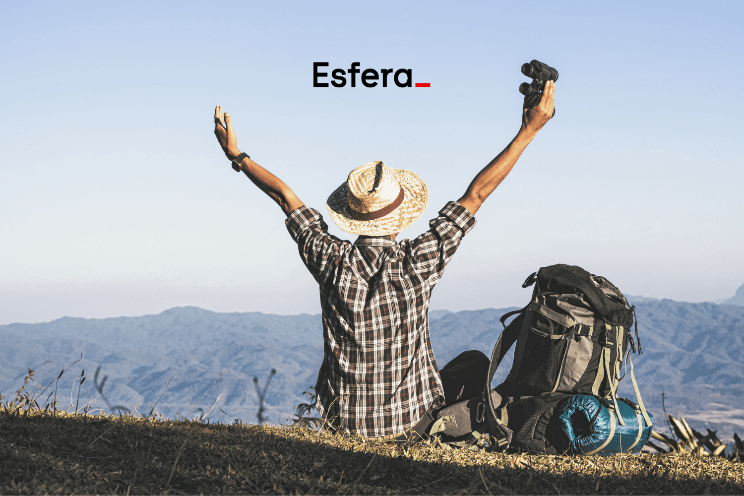 Um viajante de chapéu de palha, sentado de costas, levanta os braços em sinal de comemoração, segurando um binóculo. Ele está em uma paisagem montanhosa, com uma mochila de trilha ao seu lado. No topo da imagem, está a logo da "Esfera".