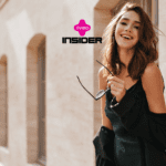 Imagem de uma mulher sorridente, caminhando ao ar livre em uma rua ensolarada, segurando óculos de sol em uma das mãos e usando um vestido leve e elegante. Na parte superior da imagem, estão as logos da Livelo e da Insider, sugerindo uma parceria entre as marcas.