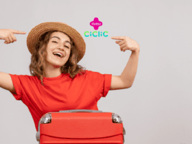 Mulher de cabelos castanhos sorridente com braços levantados e acompanhada de uma mala vermelha. Logo da Livelo e da Ciclic no canto superior da imagem