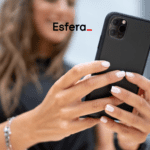 Uma mulher segura um celular preto com as duas mãos, exibindo unhas bem cuidadas e pintadas de branco. O logotipo da Esfera está centralizado na parte superior da imagem, sugerindo uma conexão entre a marca e o uso de tecnologia ou experiências digitais.