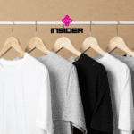 Várias camisetas básicas nas cores branca, cinza e preta estão penduradas em cabides de madeira em uma arara. Acima delas, os logotipos da Livelo e da Insider indicam uma colaboração, sugerindo produtos de moda simples e funcionais, com potencial acúmulo de pontos ou benefícios para os clientes dessas marcas.