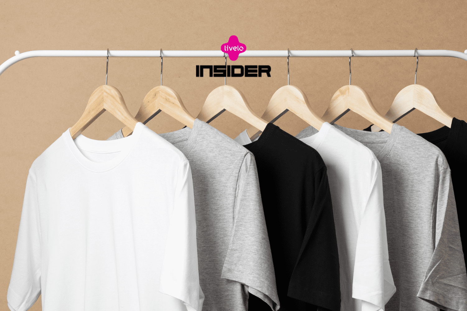 Várias camisetas básicas nas cores branca, cinza e preta estão penduradas em cabides de madeira em uma arara. Acima delas, os logotipos da Livelo e da Insider indicam uma colaboração, sugerindo produtos de moda simples e funcionais, com potencial acúmulo de pontos ou benefícios para os clientes dessas marcas.