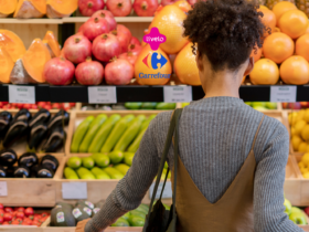 A imagem mostra uma pessoa de costas, aparentemente fazendo compras em uma seção de frutas e vegetais frescos. As prateleiras estão repletas de produtos como abóboras, romãs, abobrinhas e outros vegetais. No centro superior da imagem, os logotipos da Livelo e do Carrefour estão presentes, sugerindo uma parceria ou promoção entre as duas marcas.