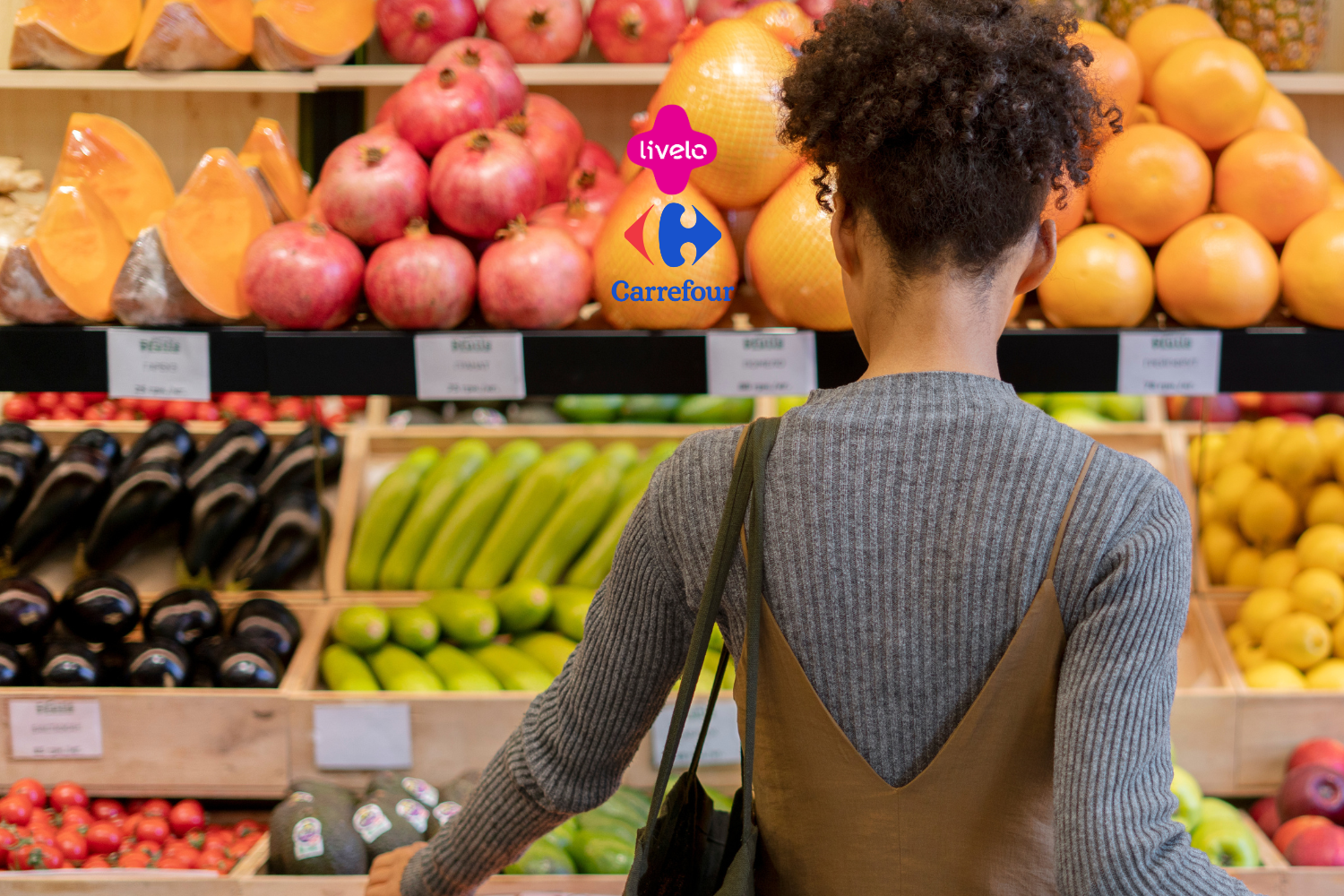A imagem mostra uma pessoa de costas, aparentemente fazendo compras em uma seção de frutas e vegetais frescos. As prateleiras estão repletas de produtos como abóboras, romãs, abobrinhas e outros vegetais. No centro superior da imagem, os logotipos da Livelo e do Carrefour estão presentes, sugerindo uma parceria ou promoção entre as duas marcas.