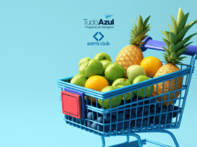 Um carrinho de supermercado azul, cheio de frutas como abacaxis, maçãs e laranjas, sobre um fundo azul claro. Acima do carrinho, estão as logos do programa de vantagens TudoAzul e do Sam's Club.