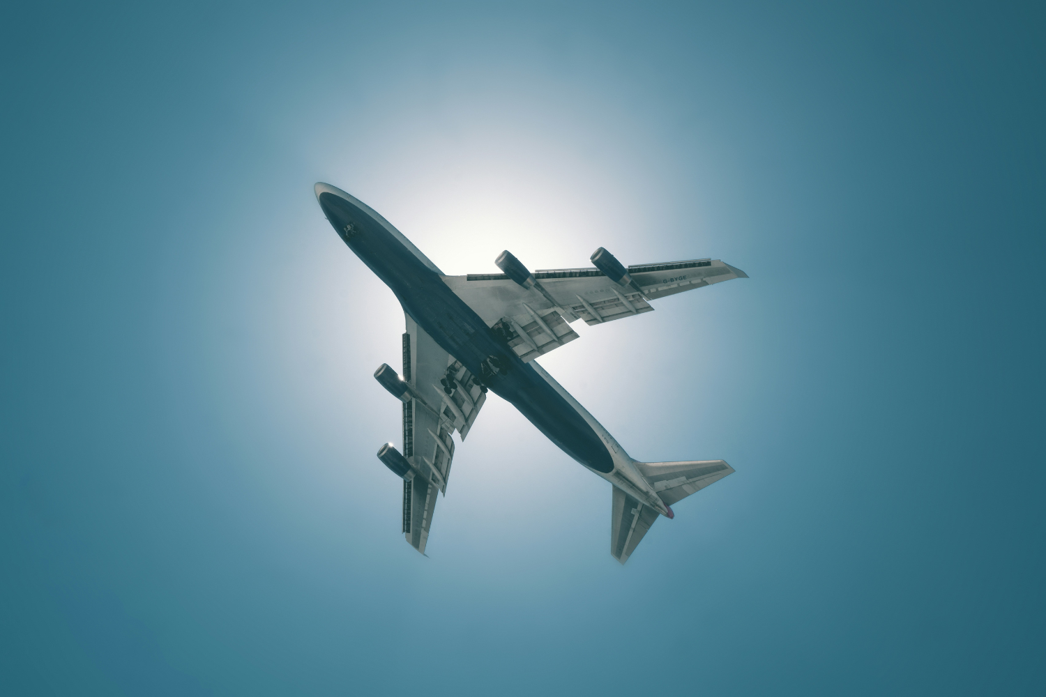Avião em voo visto de baixo, com o sol iluminando o céu azul claro ao fundo, capturando o momento de decolagem ou aterrissagem. aeroporto de porto alegre