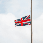 Bandeira do Reino Unido hasteada em um mastro, ondulando ao vento contra um fundo de céu nublado.