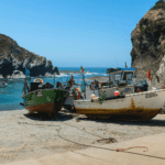 Barcos de pesca ancorados em pequena enseada rochosa com águas azuis cristalinas, cercada por falésias, na região costeira próxima a Beja, Portugal. ótima opção para o que fazer em Beja, Portugal.