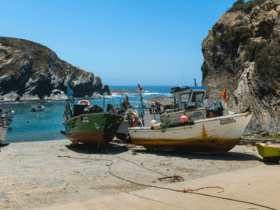 Barcos de pesca ancorados em pequena enseada rochosa com águas azuis cristalinas, cercada por falésias, na região costeira próxima a Beja, Portugal. ótima opção para o que fazer em Beja, Portugal.