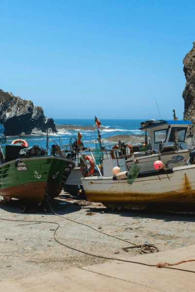 Barcos de pesca ancorados em pequena enseada rochosa com águas azuis cristalinas, cercada por falésias, na região costeira próxima a Beja, Portugal. ótima opção para o que fazer em Beja, Portugal.