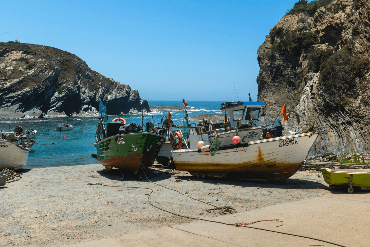 Barcos de pesca ancorados em pequena enseada rochosa com águas azuis cristalinas, cercada por falésias, na região costeira próxima a Beja, Portugal. ótima opção para o que fazer em Beja, Portugal.