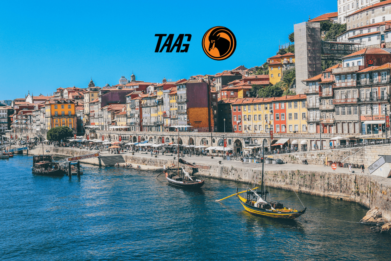 Vista do Cais da Ribeira, na cidade do Porto, Portugal, com barcos tradicionais no Rio Douro e fachadas coloridas ao fundo, acompanhada do logotipo da TAAG Angola Airlines no céu azul.