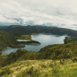 Vista panorâmica da Lagoa do Fogo cercada por montanhas verdes e céu nublado, um dos cenários mais emblemáticos de onde fica a Ilha de São Miguel, em Portugal.