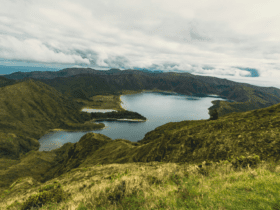 Vista panorâmica da Lagoa do Fogo cercada por montanhas verdes e céu nublado, um dos cenários mais emblemáticos de onde fica a Ilha de São Miguel, em Portugal.